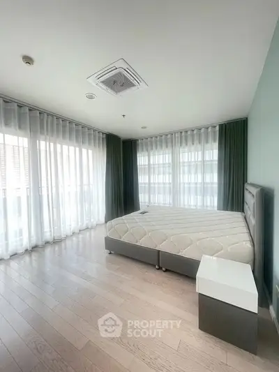 Spacious bedroom with large windows and modern furnishings in a bright apartment.