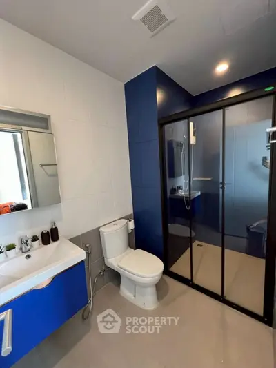 Modern bathroom with sleek blue and white design, featuring a glass shower enclosure and stylish fixtures.