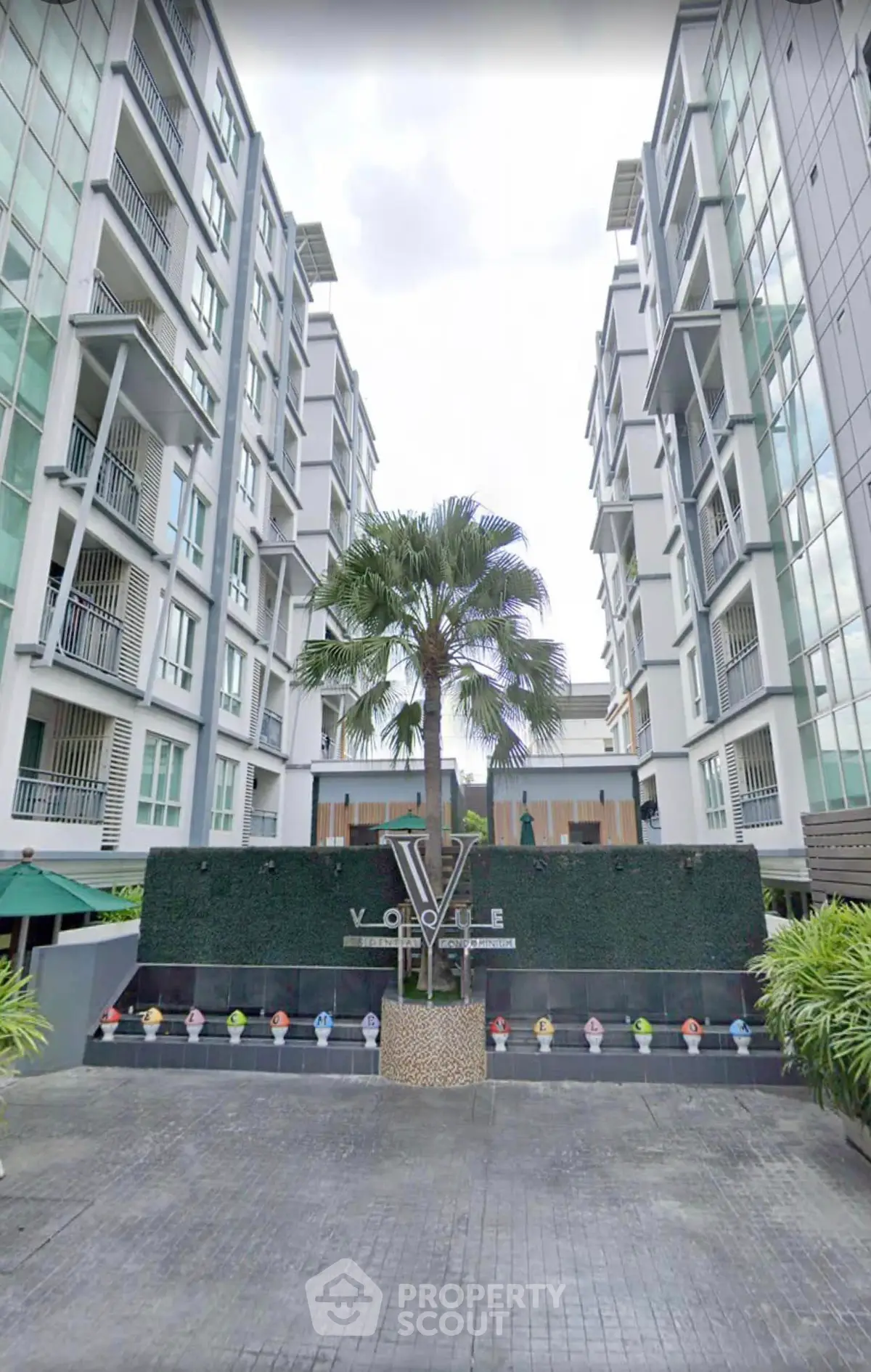 Modern apartment building exterior with lush landscaping and palm tree centerpiece.