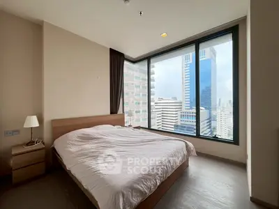 Modern bedroom with large windows offering stunning city views in a high-rise building.