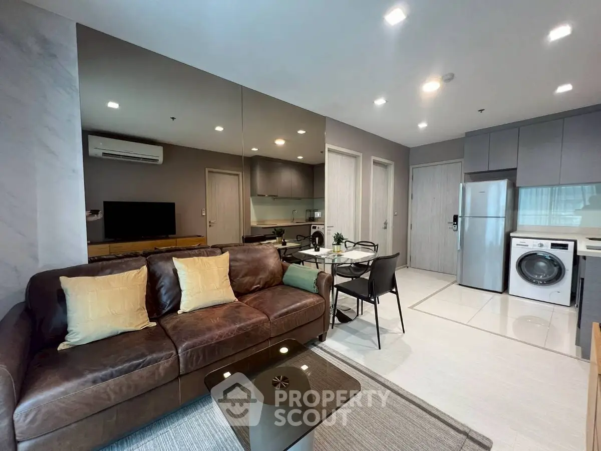 Modern living room with leather sofa, dining area, and sleek kitchen in open layout apartment.