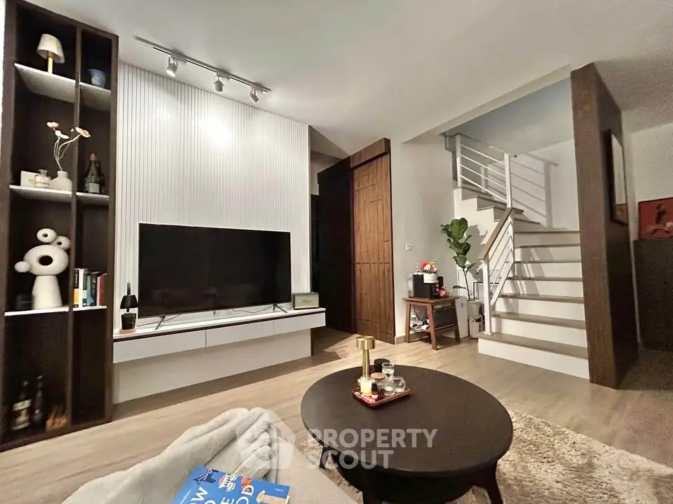 Modern living room with stylish decor and staircase, featuring a sleek TV unit and cozy seating area.