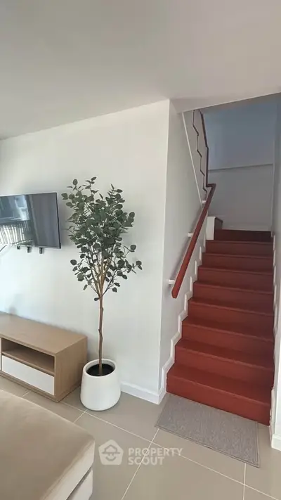 Modern living room with red staircase and wall-mounted TV, featuring a stylish potted plant.