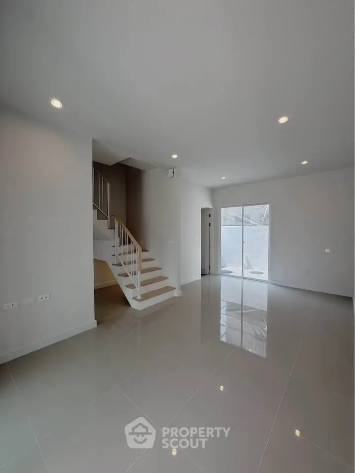 Spacious modern living room with sleek staircase and large windows for natural light.