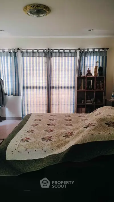 Cozy bedroom with floral quilt and striped curtains, perfect for relaxation.