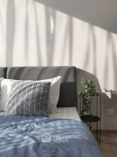 Cozy bedroom with stylish decor and natural light, featuring a plush bed and elegant plant accent.