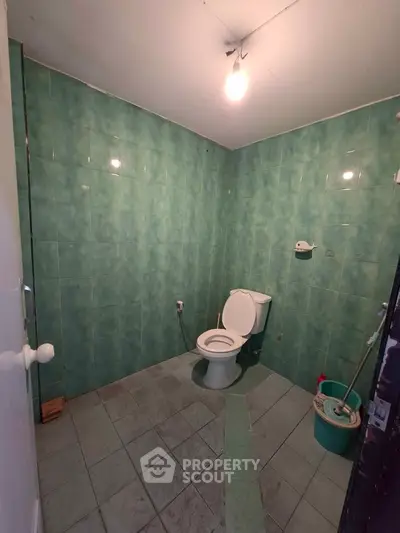 Spacious bathroom with green tiled walls and a toilet, ideal for renovation.