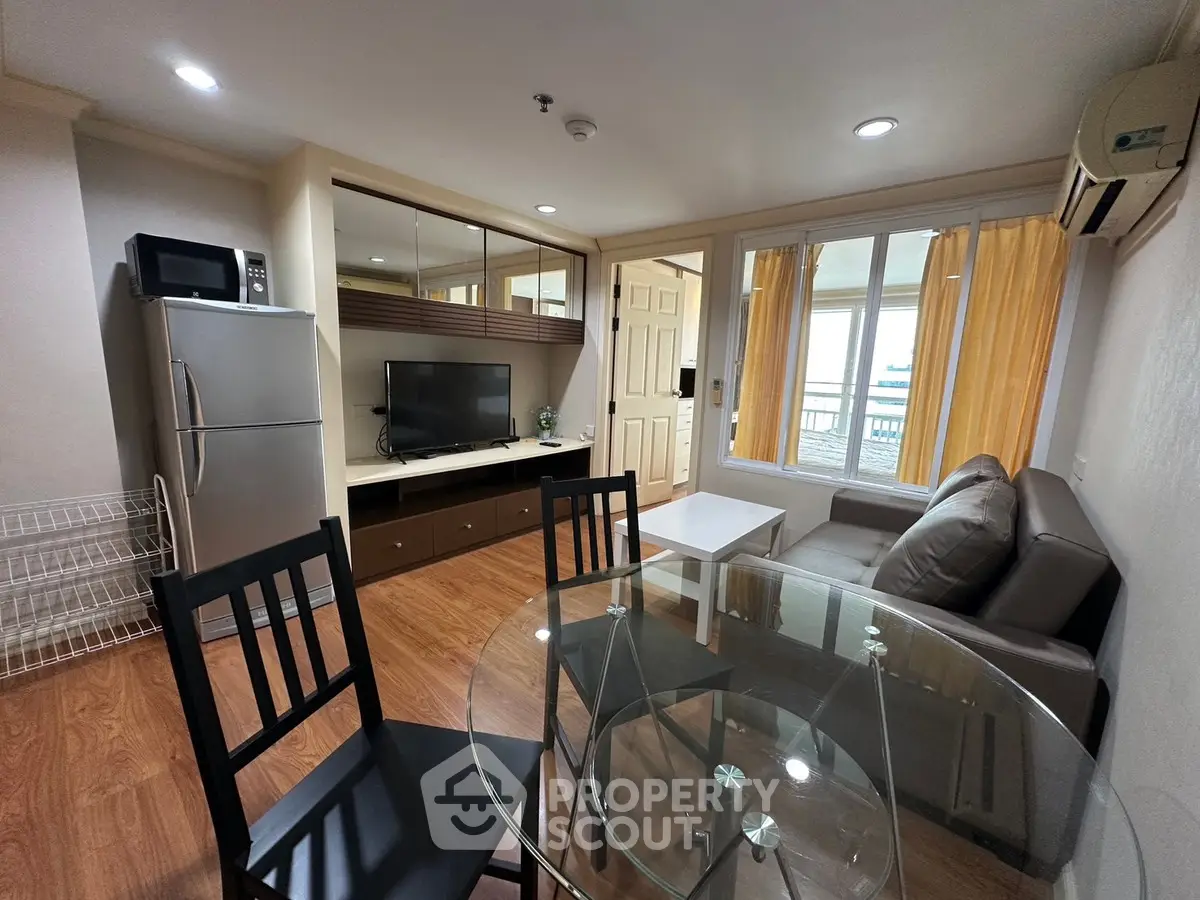 Modern living room with glass dining table, cozy sofa, and sleek kitchen appliances in a stylish apartment.