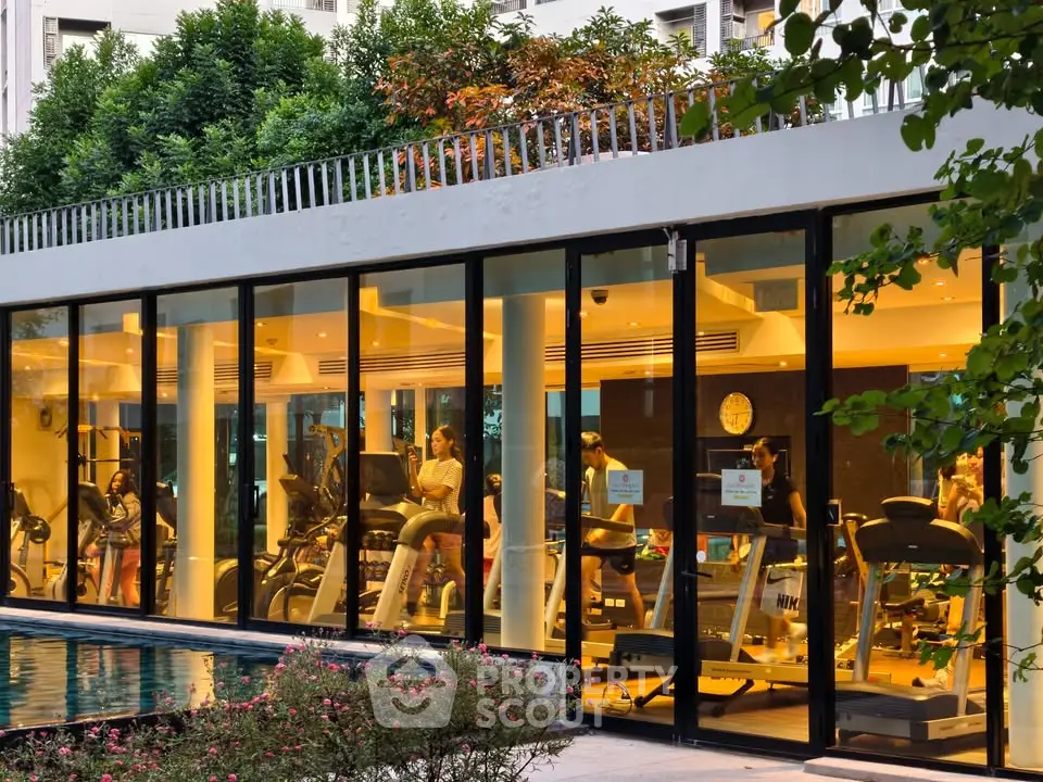 Modern gym with glass walls overlooking a serene pool in a luxury residential complex.