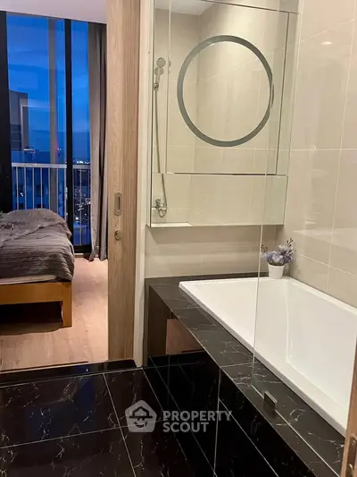 Luxurious bathroom with modern bathtub and view into elegant bedroom with cityscape backdrop.