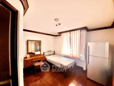 Cozy bedroom with wooden furniture and natural light, featuring a bed, dresser, and refrigerator.