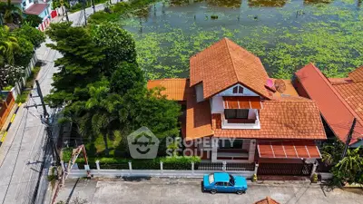 Charming suburban house with red roof and lush garden by a serene pond.