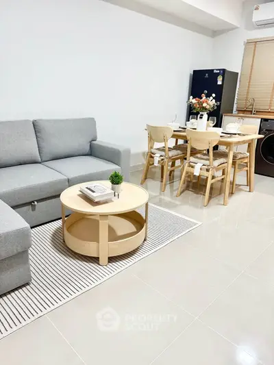 Modern living room with cozy gray sofa and dining area, featuring sleek furniture and bright tiled flooring.