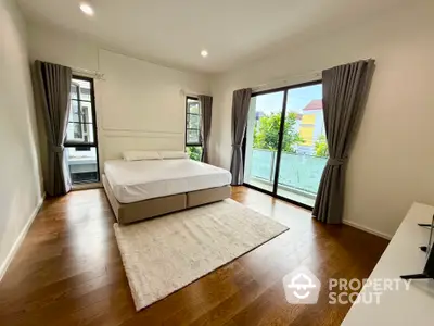 Spacious bedroom with large windows and balcony access, featuring elegant hardwood floors and modern decor.