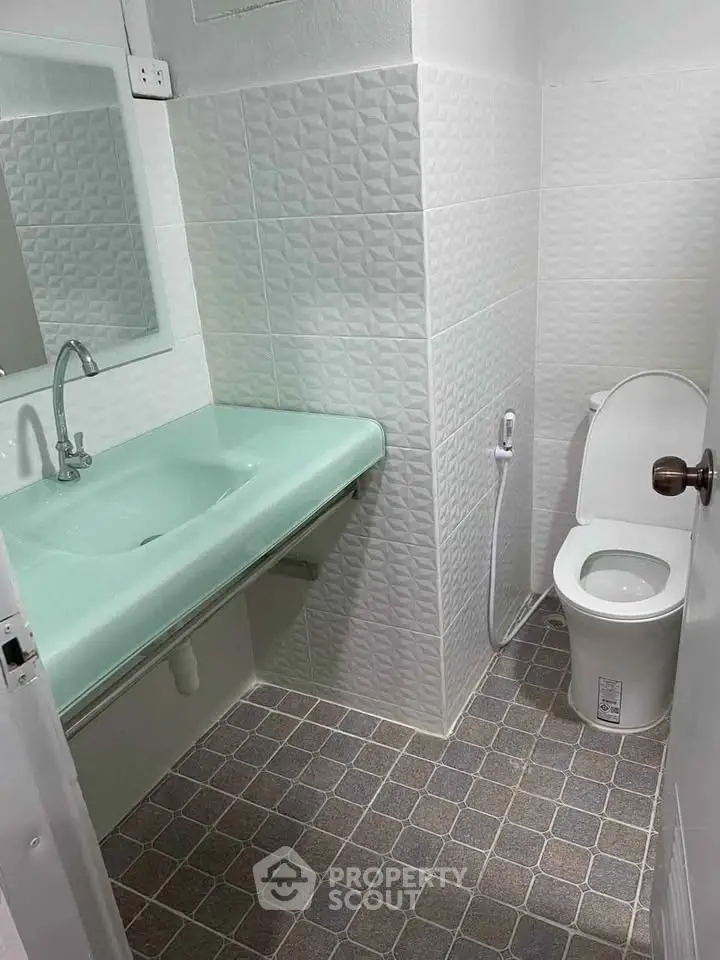 Modern bathroom with sleek green sink and white tiled walls, featuring a compact toilet and stylish fixtures.