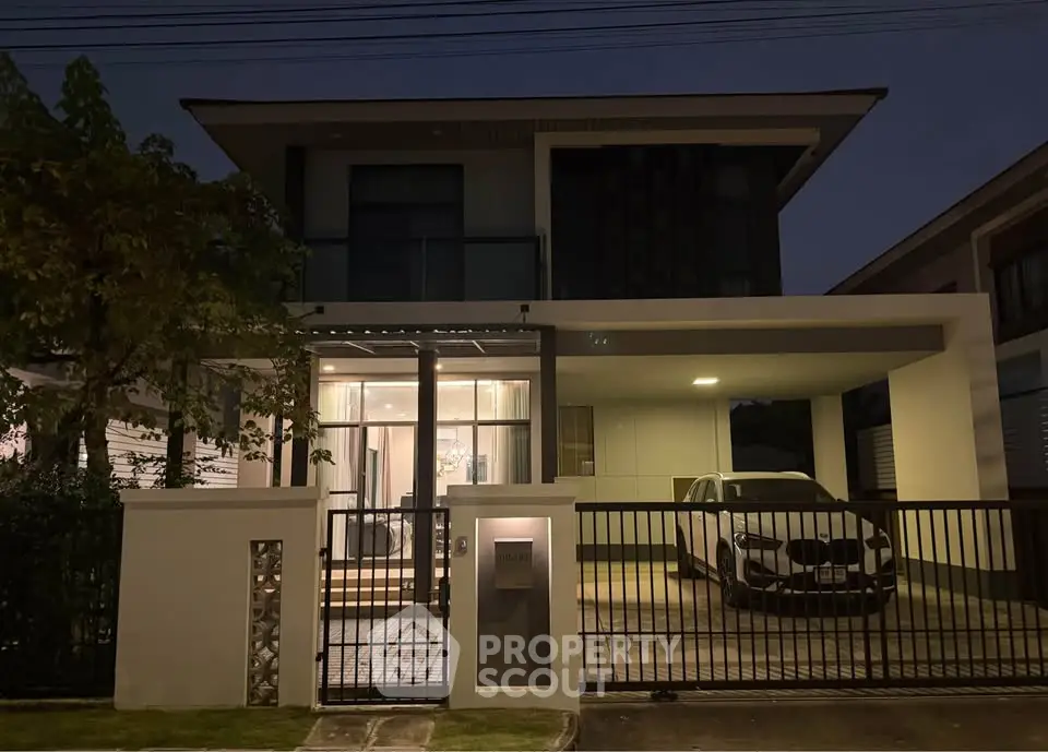 Modern two-story house with sleek design and car parked in driveway, illuminated at night.