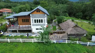 Charming countryside property with modern house and traditional thatched-roof hut surrounded by lush greenery.