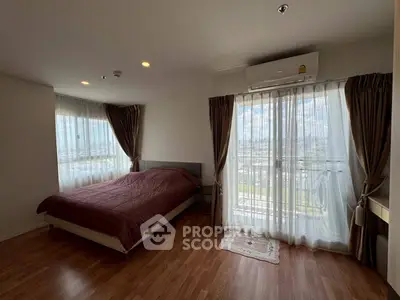 Spacious bedroom with large windows and city view, featuring elegant curtains and wooden flooring.