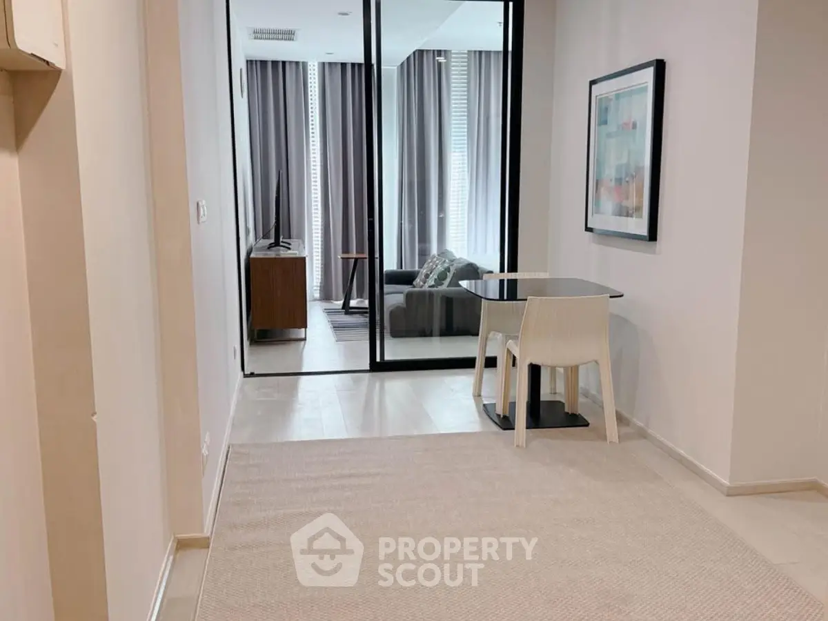 Modern apartment hallway leading to a stylish living room with sleek furniture and large windows.