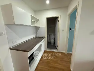 Compact kitchen with wooden flooring and adjacent bathroom in modern apartment