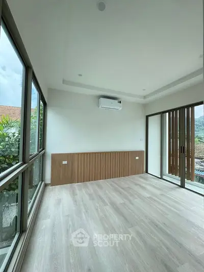 Spacious modern room with large windows and scenic view, featuring sleek wooden flooring and air conditioning.