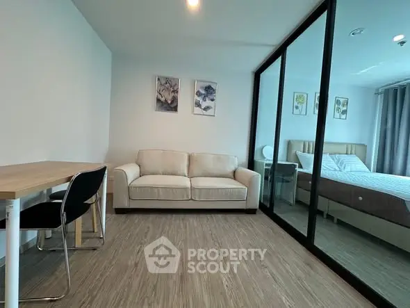 Modern apartment interior with cozy living room and bedroom separated by glass wall.