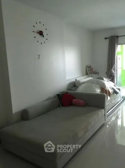 Modern living room with sleek sofa and wall clock, featuring glossy floors and natural light.