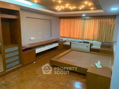 Spacious bedroom with wooden flooring and built-in furniture, featuring a cozy seating area and ambient lighting.