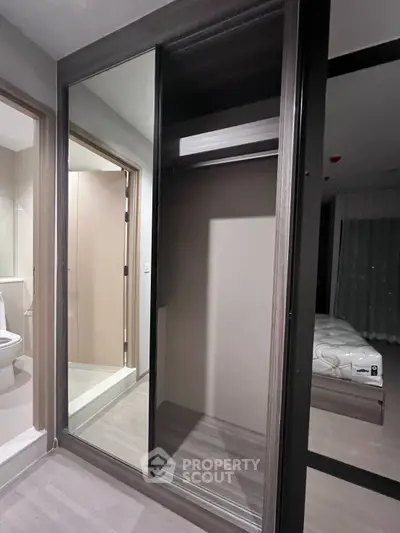 Modern bedroom with sliding mirrored wardrobe and adjacent bathroom entrance.