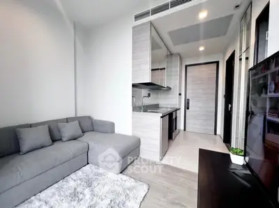 Modern living room with sleek kitchen in open layout, featuring cozy gray sofa and stylish decor.