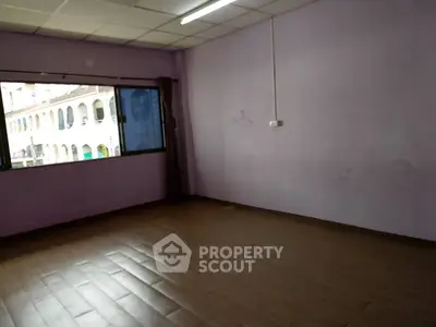Spacious empty room with large window and wooden flooring, ideal for customization.