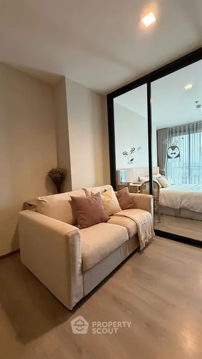 Modern living room with cozy sofa and glass partition leading to stylish bedroom.