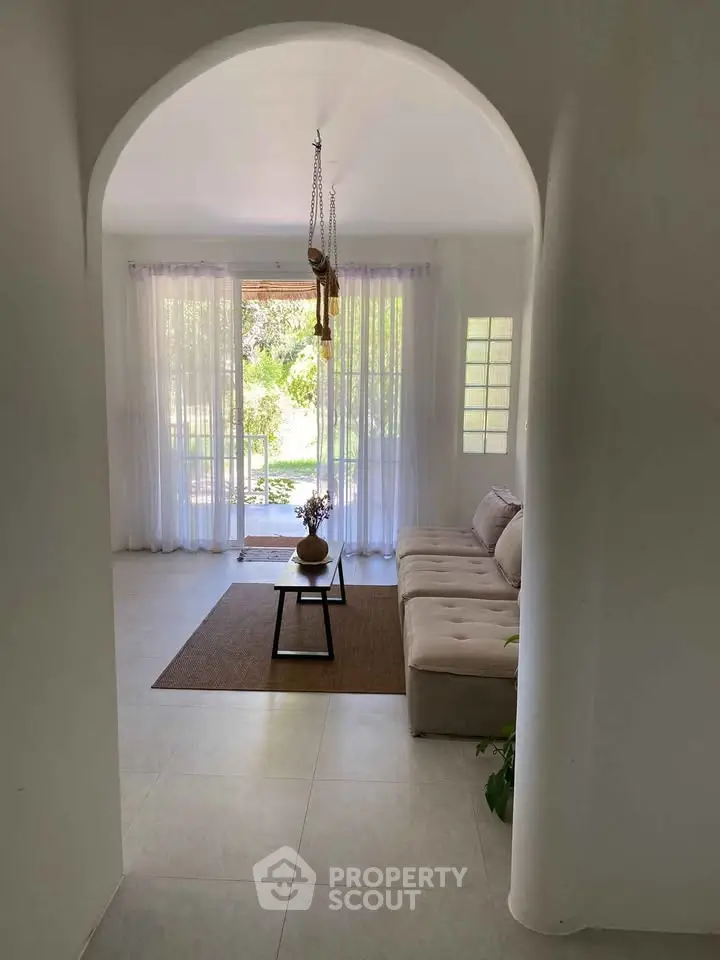 Elegant living room with archway entrance, cozy sofa, and large window overlooking lush greenery.