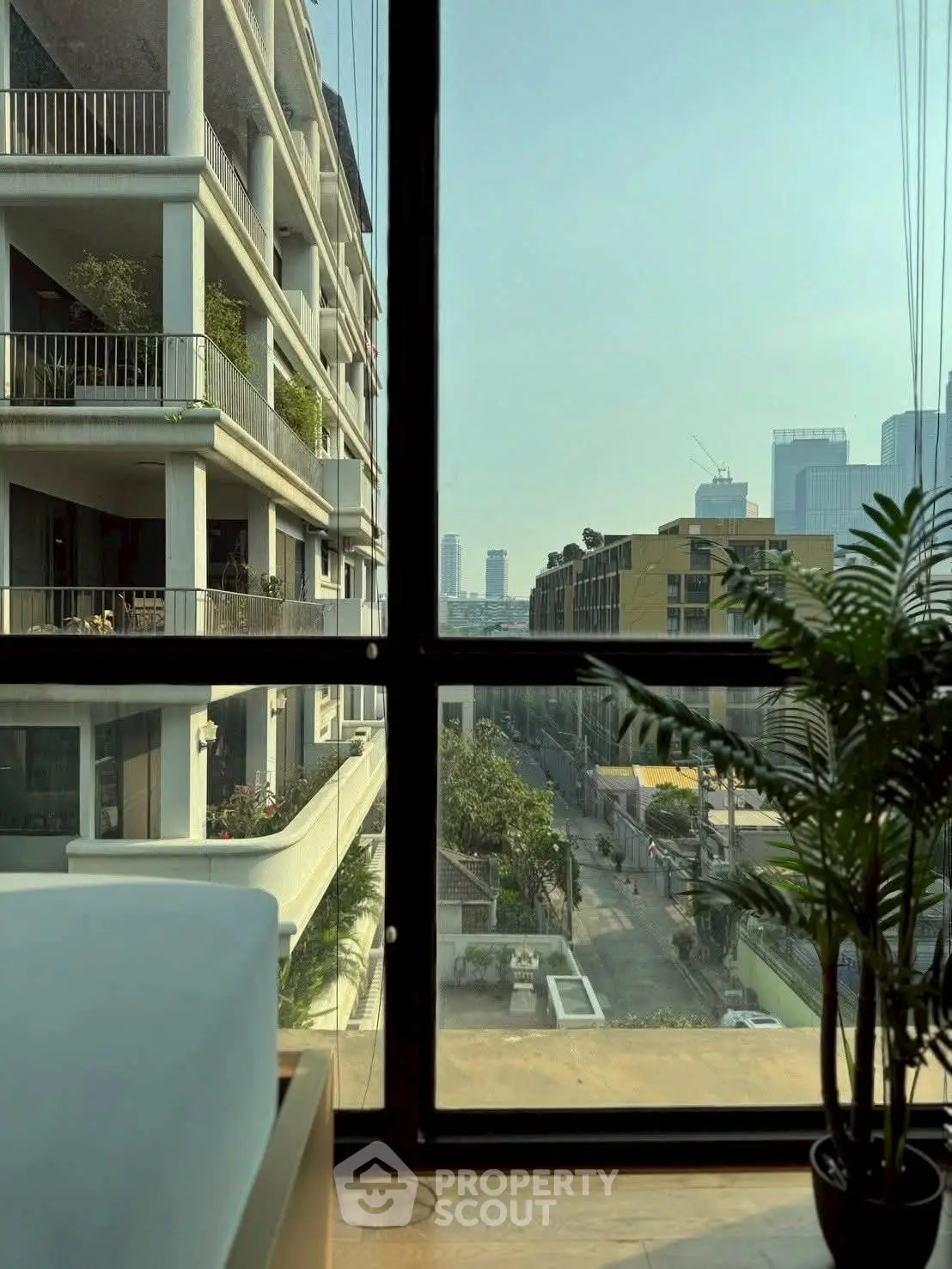 Stunning urban view from modern apartment window with city skyline and lush greenery.