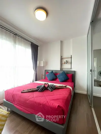Cozy bedroom with vibrant red bedding and natural light, featuring modern decor and wooden flooring.