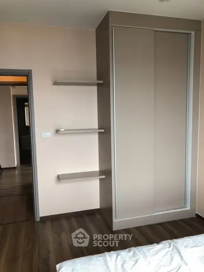 Modern bedroom with sleek built-in wardrobe and floating shelves, featuring elegant wood flooring.