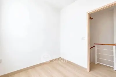 Minimalist interior with wooden flooring and open doorway leading to staircase.