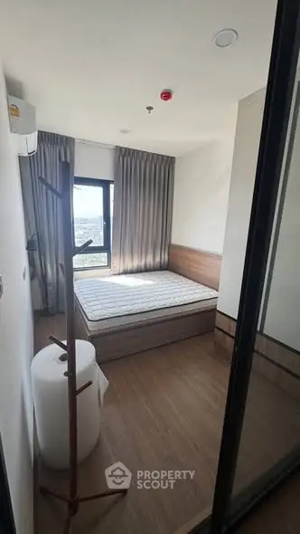 Cozy bedroom with wooden flooring and large window offering natural light.