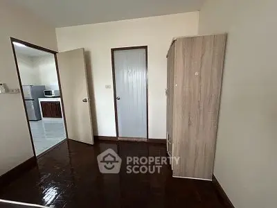 Spacious room with wooden flooring and a view into a modern kitchen area.