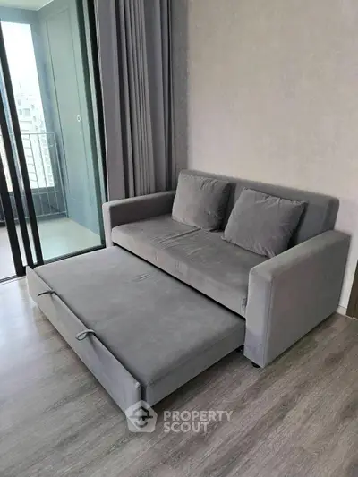 Modern living room with sleek gray sofa bed and balcony view, perfect for urban living.