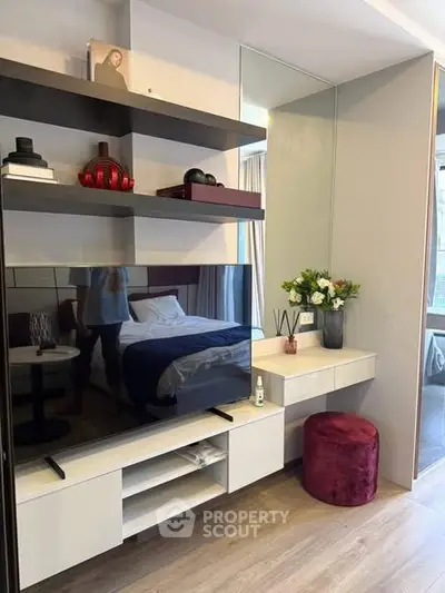 Modern bedroom with stylish decor, featuring a TV, shelves, and a cozy seating area.