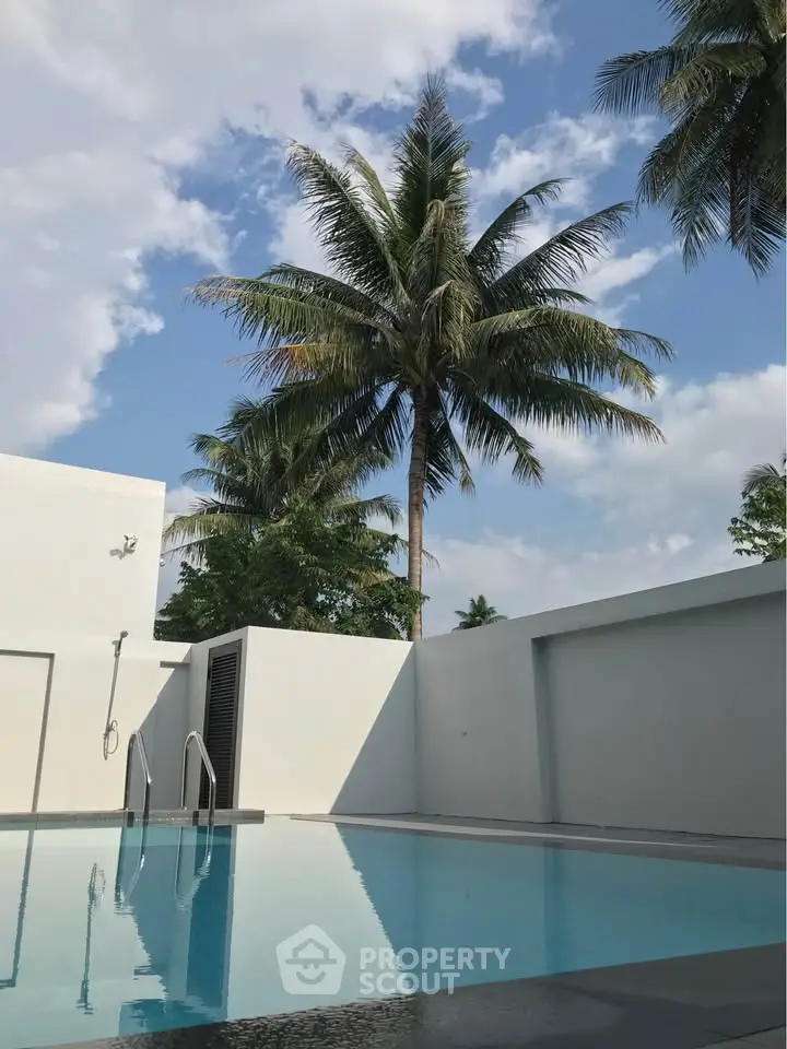 Luxurious outdoor pool area with palm trees and clear blue sky, perfect for relaxation and leisure.