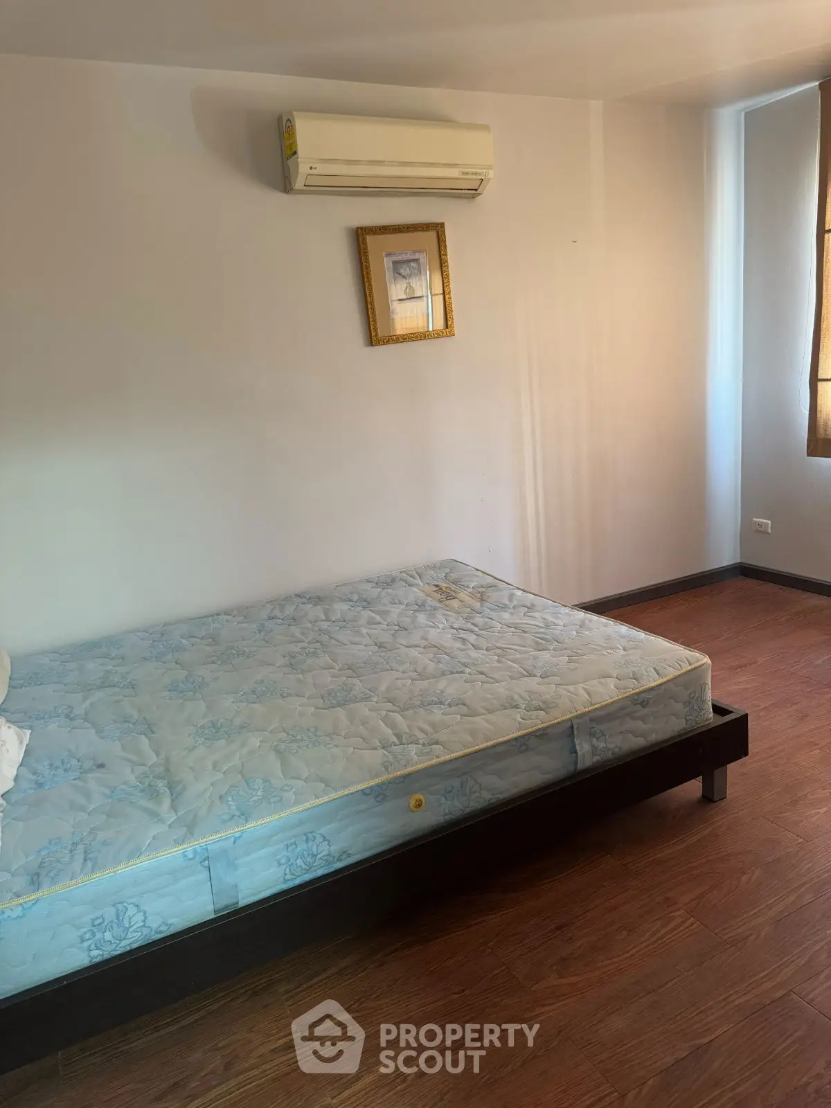 Cozy bedroom with wooden flooring and wall-mounted air conditioner, perfect for a comfortable living space.