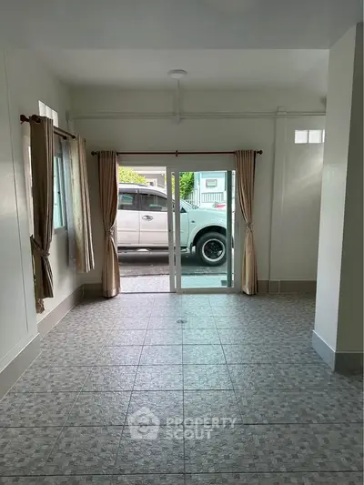 Spacious living room with tiled flooring and sliding glass doors leading to driveway.