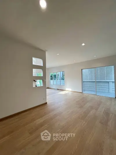 Spacious modern living room with wooden flooring and large windows for natural light.