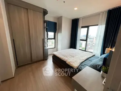 Modern bedroom with large windows and city view, featuring sleek wooden flooring and stylish furnishings.