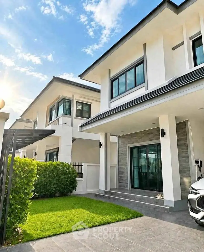 Modern two-story house with sleek design and lush green lawn under a bright blue sky.