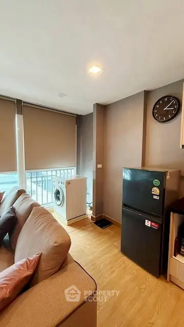 Modern living room with washing machine and fridge, featuring cozy sofa and large windows.