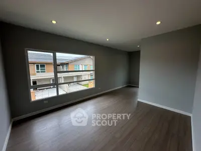Spacious modern room with large window and wooden flooring, perfect for versatile living space.