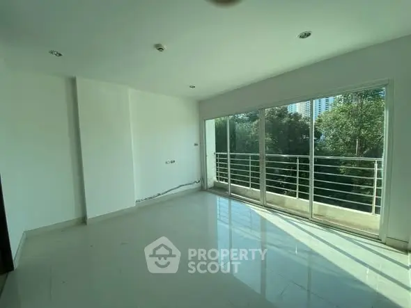 Spacious empty room with large windows and balcony overlooking greenery.